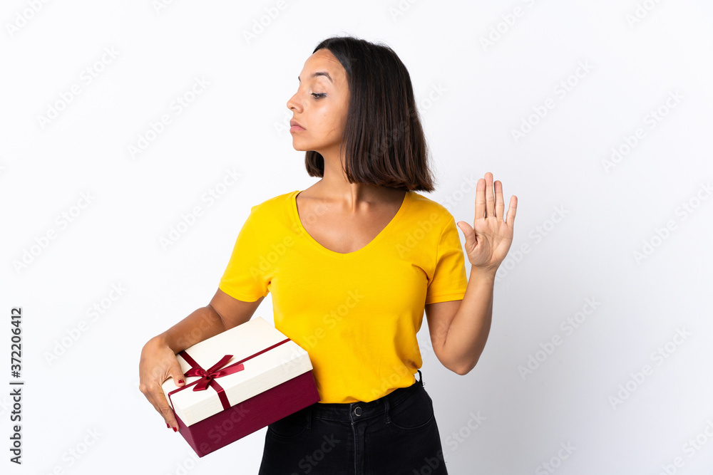 Young latin woman holding a gift isolated on white background making stop gesture and disappointed Young latin woman holding a gift isolated on white background making stop gesture and disappointed