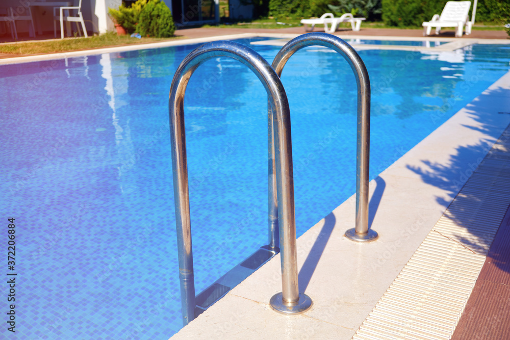 Hand rails of swimming pool. Metal entry ladder of swimming pool