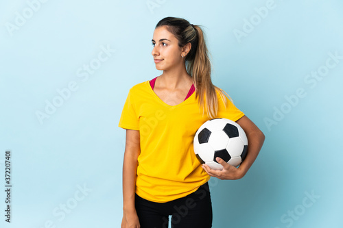 Young hispanic football player woman over isolated on blue background looking to the side © luismolinero