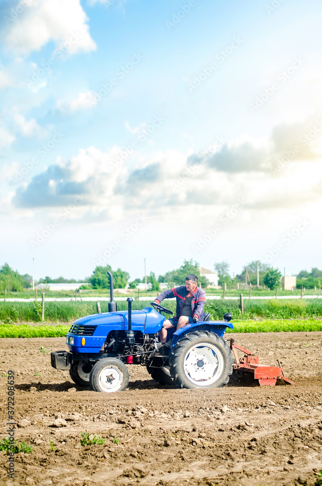 Obraz premium The farmer drives a tractor with a milling unit equipment. Loosening land cultivation Use of agricultural machinery to speed up work. Farming. Plowing field. The stage of preparing soil for planting.