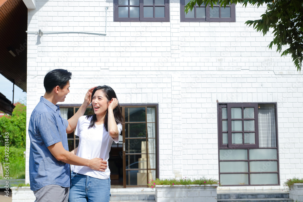 Asian male and female couples stand, hug, and smile happily in front of the new house. The concept of starting a married life In order to create a happy family. copy space