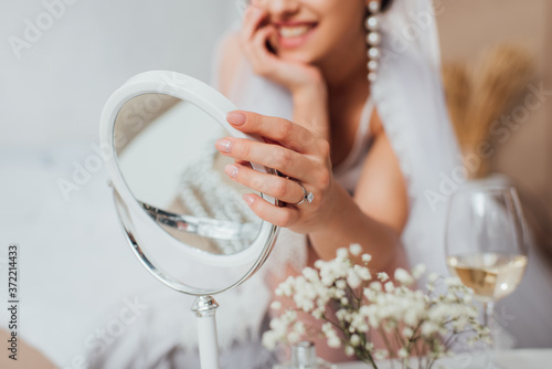 Cropped view of bride touching mirror near flowers and glass on wine