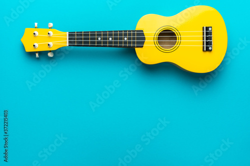 Yellow colored wooden ukulele guitar on the turquoise blue background. Overhead photo of ukulele with copy space.