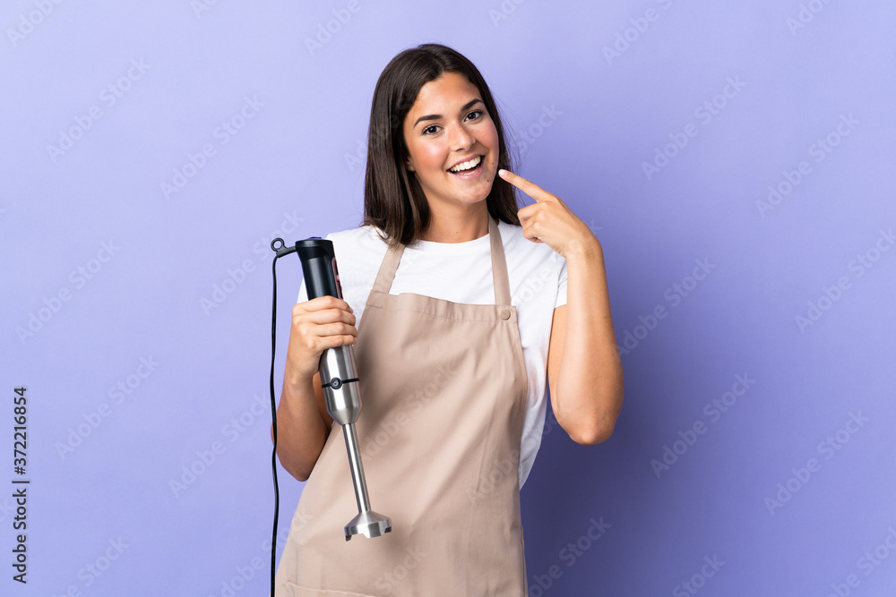 Brazilian woman using hand blender isolated on purple background giving a thumbs up gesture Brazilian woman using hand blender isolated on purple background giving a thumbs up gesture