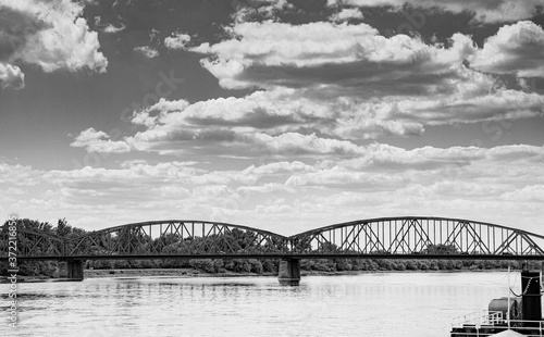 Black and white vintage photography road bridge over Vistula River in Torun (Pilsudski Bridge), Poland. Heavy rusty steel old industrial vehicle overpass. Landscape city view from boulevard.