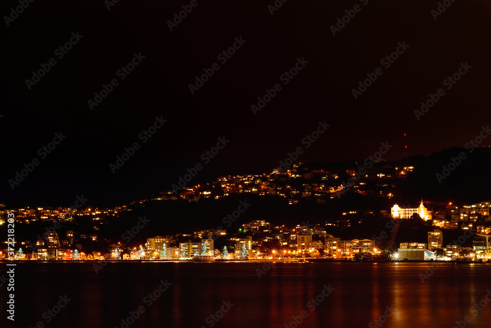Wellington city at night: Lit-up houses on the slopes of Mt Victoria and street lights reflected in calm water of Wellington Harbour. Selective focus