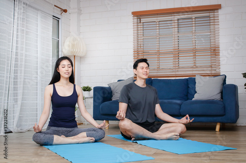 Asian couples do yoga exercises at home together during COVID-19 and social distancing. Concept of keeping healthy. copy space