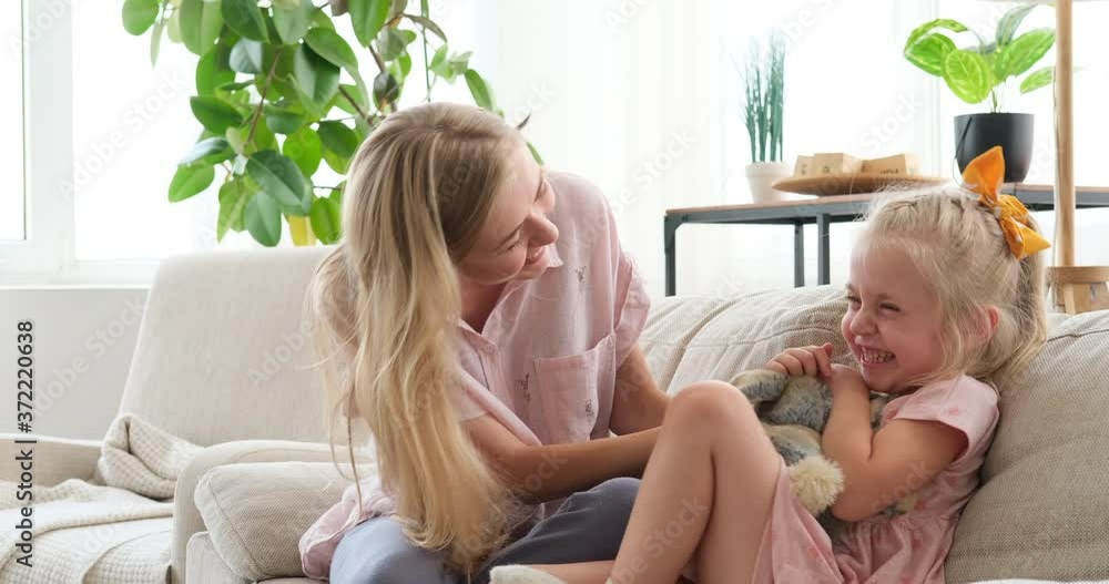 Playful mother having fun tickling little daughter on sofa at home Playful mother having fun tickling little daughter on sofa at home
