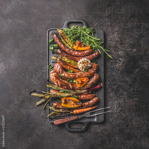 Canvas Print Grilled food on cast iron plate: sausage, pepper, spring onion, garlic, paprika, herbs, carrot with meet fork
