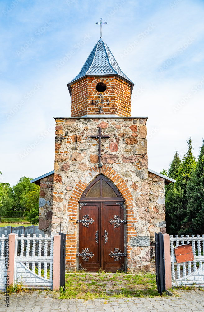 Fototapeta premium Small vintage christian catholic chapel. Brick building with gothic wooden gate with fittings.Worship village building. Old religion prayer church.