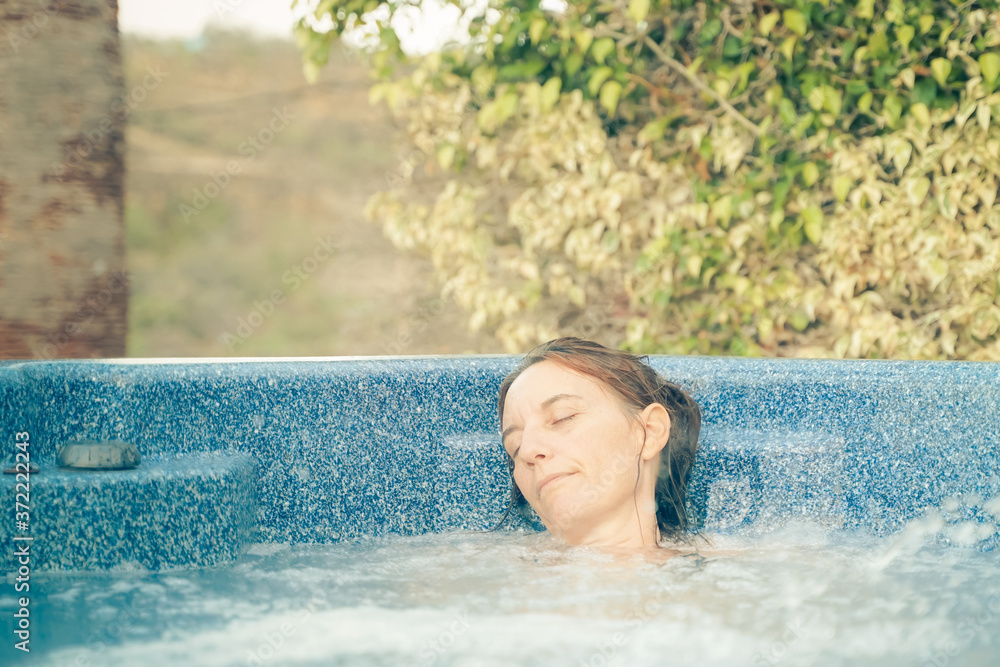 Attractive woman relaxing in a jacuzzi. Photo of happy beautiful woman in jacuzzi during vacation. Luxury lifestyle wellness spa treatment vacation recreation resort hotel service concept.
