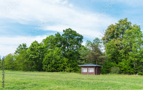 Traditional small wooden scandinavian house at the forest edge. Typical summer cottage. Countryside authentic cozy little cabin in a rural area of brown color with white windows.