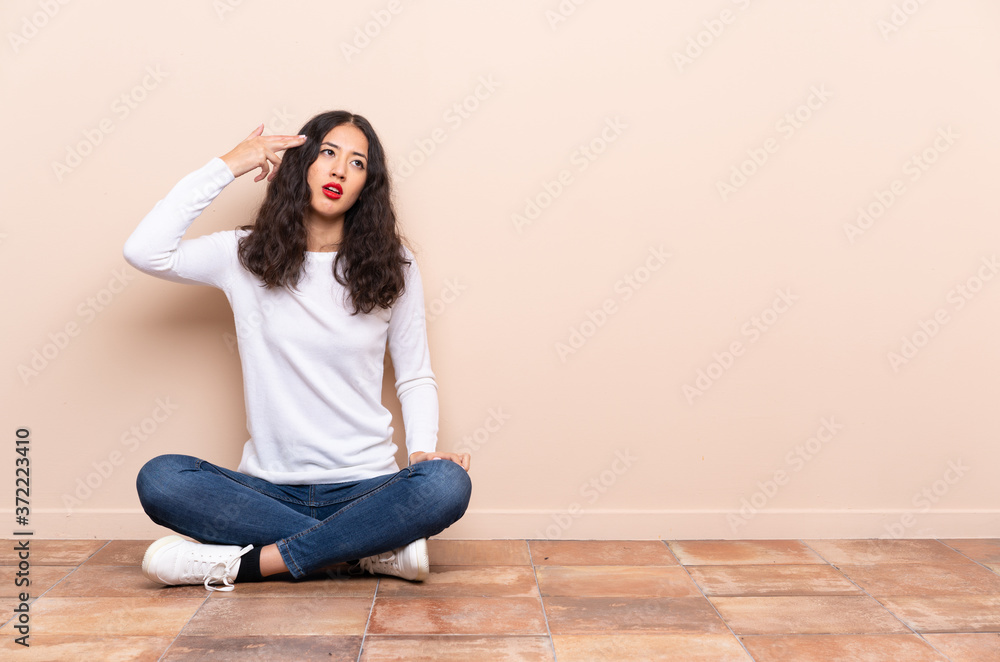 Young woman sitting on the floor with problems making suicide gesture Young woman sitting on the floor with problems making suicide gesture