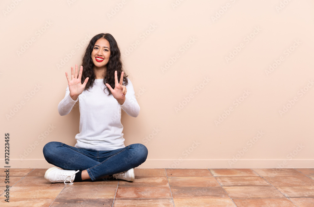 Young woman sitting on the floor counting eight with fingers Young woman sitting on the floor counting eight with fingers