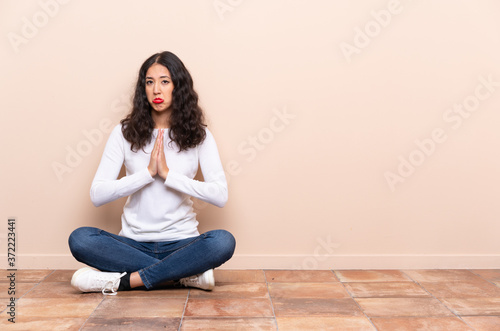 Young woman sitting on the floor keeps palm together. Person asks for something