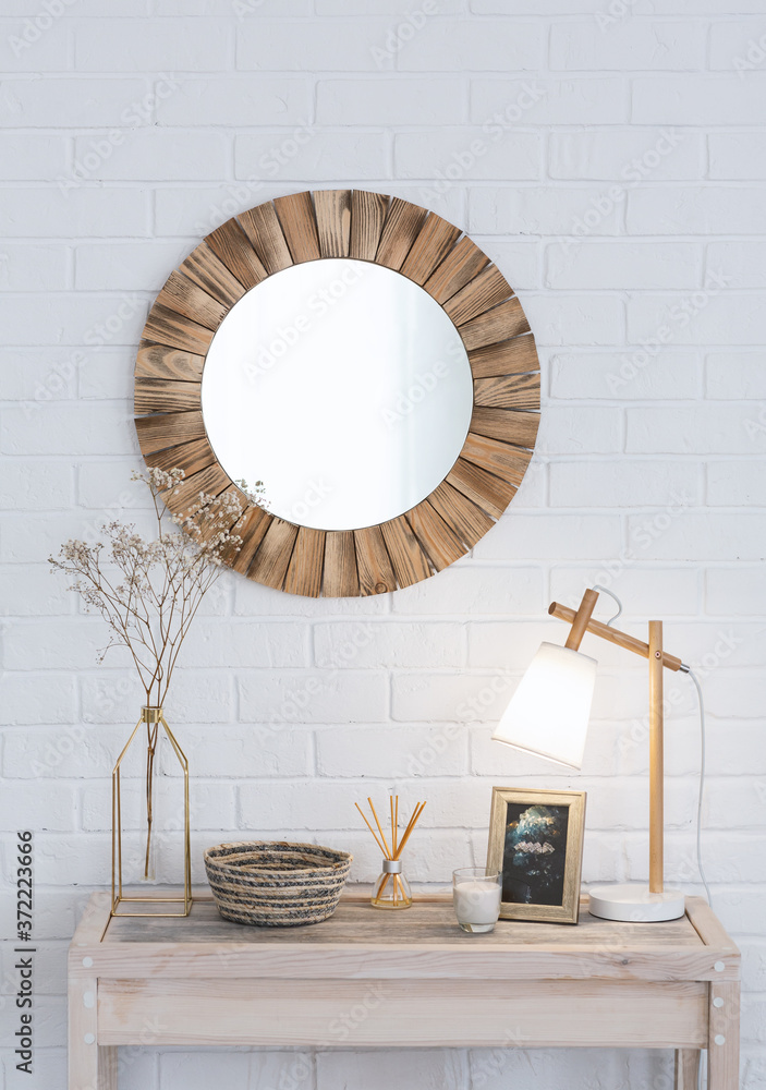 Bedroom interior. Dry bouquet in vase, aroma sticks and lamp on wooden  dressing table, and round mirror on white brick wall Stock Photo