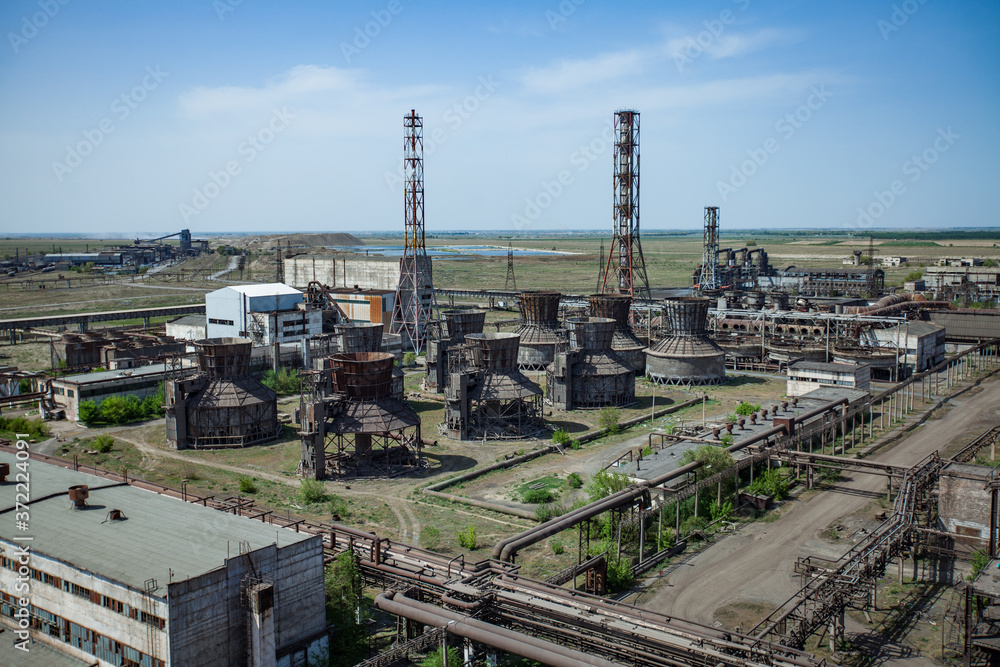 Outdated soviet metallurgy factory buildings and rusted pipelines and chimneys and cooling towers. On steppe and blue sky background. Taraz city, Kazakhstan. Outdated soviet metallurgy factory buildings and rusted pipelines and chimneys and cooling towers. On steppe and blue sky background. Taraz city, Kazakhstan.