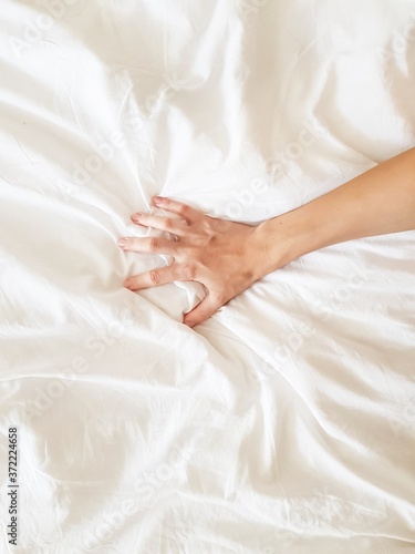 Close up sexy woman hand pulling and squeezing white sheets in ecstasy in bed. Orgasm on white bed. Sex and erotic concept.