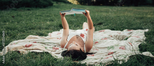 Canvas-taulu Wide angle shot of young woman lying on the soft coverlet and reading a book