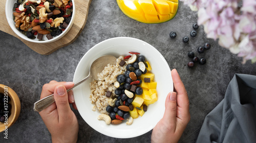 Oatmeal with dried fruits, nuts and mango. Woman's hands holding plate, eating healthy breakfast. lthy breakfast, dieting and nutrition. photo