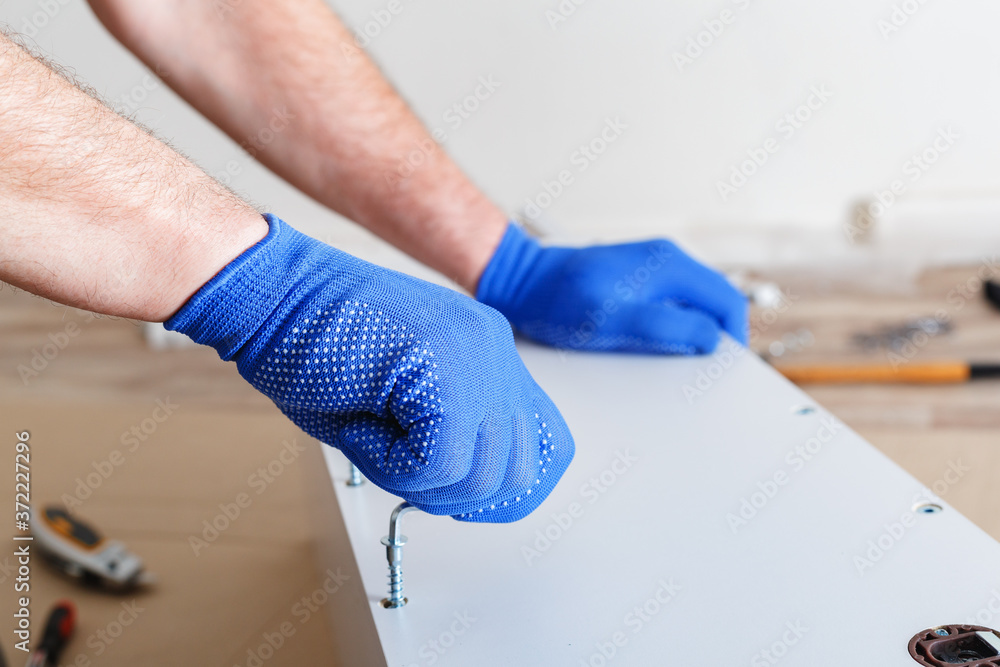 Furniture assembly. Male hands in gloves master collects furniture using screwdriver tools, instrument at home. Moving, home improvement, furniture repair and renovation. Closeup
