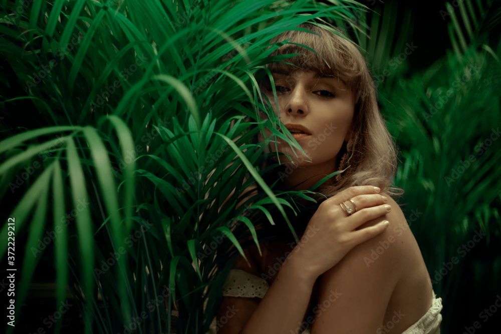 Woman in palm leaves. Model's face in green. Fashion photo of a girl in the tropics Woman in palm leaves. Model's face in green. Fashion photo of a girl in the tropics