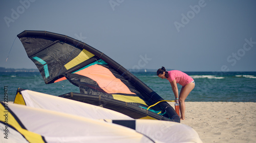 Middle-aged woman pumping up up a kitesurfing kite at the beach on summer vacation in hot sunshine with ocean backdrop