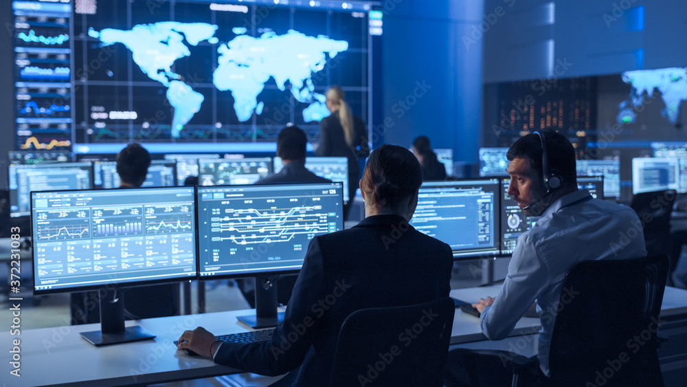 Team of Professional Computer Data Science Engineers Work on Desktops with Screens Showing Charts, Graphs, Infographics, Technical Business Data and Statistics. Low Key Control and Monitoring Room. Team of Professional Computer Data Science Engineers Work on Desktops with Screens Showing Charts, Graphs, Infographics, Technical Business Data and Statistics. Low Key Control and Monitoring Room.