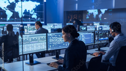 Team of Professional Computer Data Science Engineers Work on Desktops with Screens Showing Charts, Graphs, Infographics, Technical Business Data and Statistics. Dark Control and Monitoring Room.