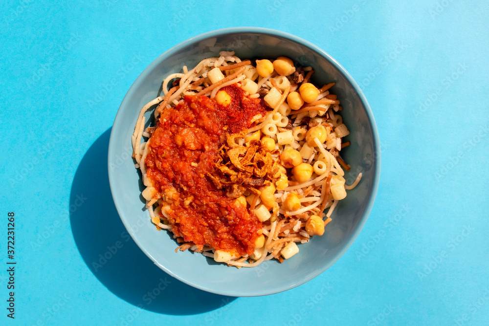 Famous traditional Arabic, Egyptian dish - Koshari. National Kushari in a turquoise plate on blue background. Top view. Famous traditional Arabic, Egyptian dish - Koshari. National Kushari in a turquoise plate on blue background. Top view.