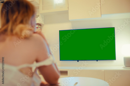 The girl sits at home in the evening on the couch in front of the TV. A woman looks at the news after work. Green monitor screen