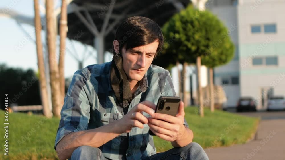 Isolated Handsome man sitting in park in medical mask and using smartphone Isolated Handsome man sitting in park in medical mask and using smartphone