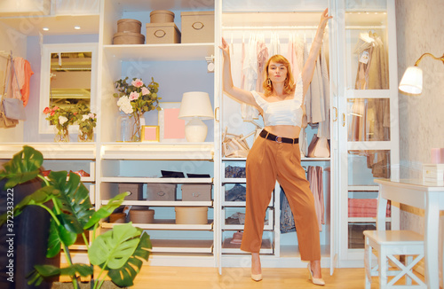 Girl model posing against the backdrop of a wardrobe with clothes. Woman in trousers and white top showing her room  gardirop