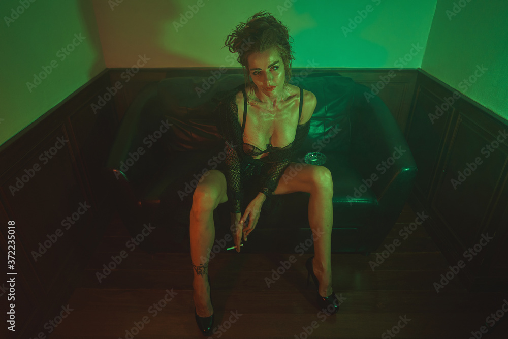 Beautiful long legged woman is posing on the couch in a green light