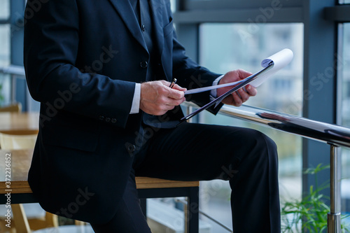 Man managing director leaned on a wooden table in his office near a large window and looks at a successful business development plan.