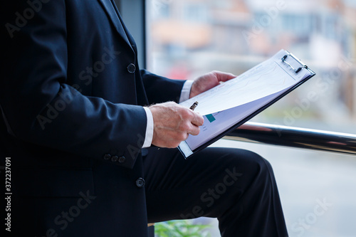 Man managing director leaned on a wooden table in his office near a large window and looks at a successful business development plan.