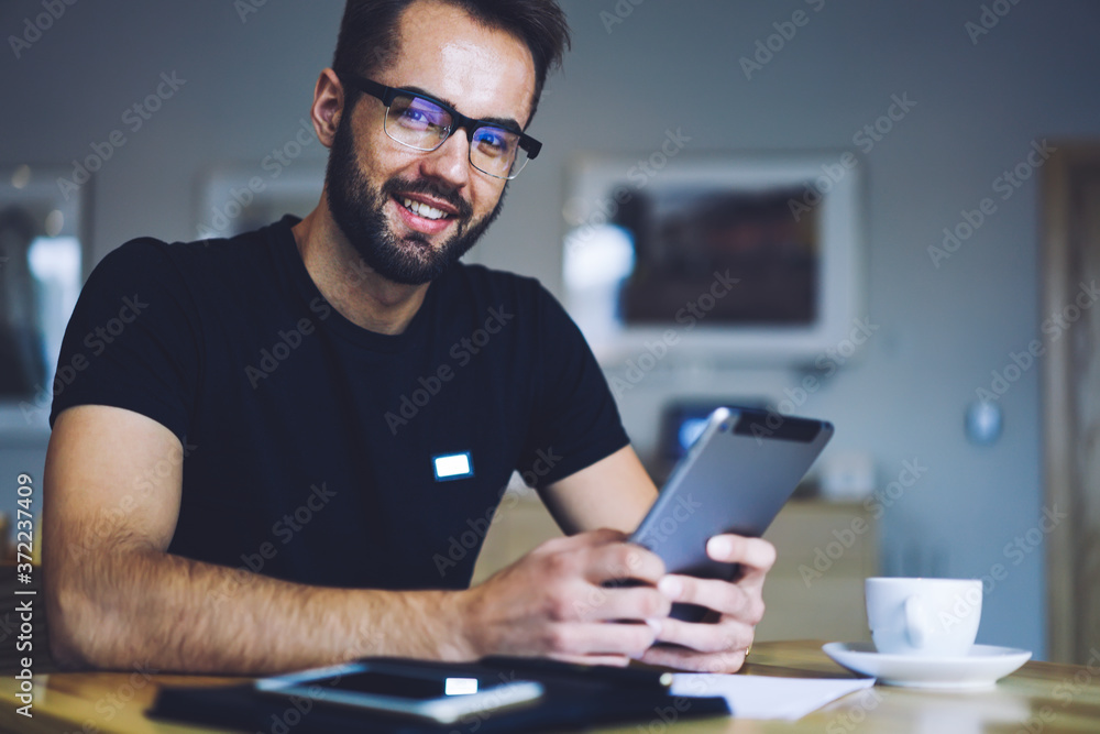 Half length portrait of smiling handsome man in cool spectacles chatting with friends in social network on touchpad connected to wifi. Positive good looking businessman spending free time in cafeteria Half length portrait of smiling handsome man in cool spectacles chatting with friends in social network on touchpad connected to wifi. Positive good looking businessman spending free time in cafeteria