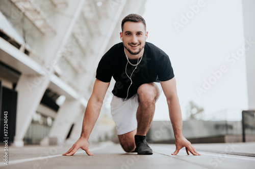 young smiling handsome brunette man in sportswear on ready position to run on the street stadium listens his favorite music, healthy fit lifestyle