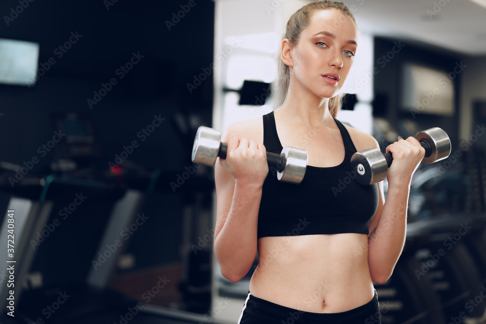 Young brunette sporty woman exercising with dumbbell in a gym Young brunette sporty woman exercising with dumbbell in a gym