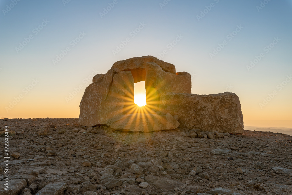 Ταπετσαρία Rising  sun rays pass through a large stone dolmen at dawn in a public sculpture park in the desert, on a cliff above the Judean Desert near Mitzpe Ramon in Israel