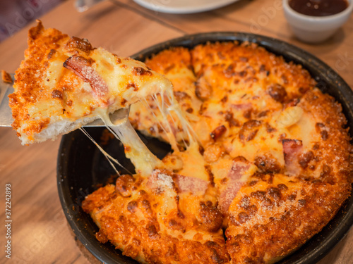 cheese pizza on wooden board. slid pieace growing cheddar cheese, restaurant table. fastfood concept photo