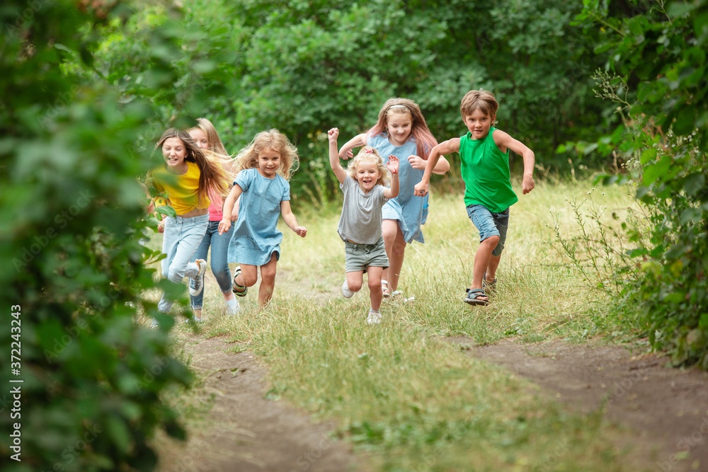 Fototapeta premium Happiness. Kids, children running on green forest. Cheerful and happy boys and girs playing, laughting, running through green blooming meadow. Childhood and summertime, sincere emotions concept.