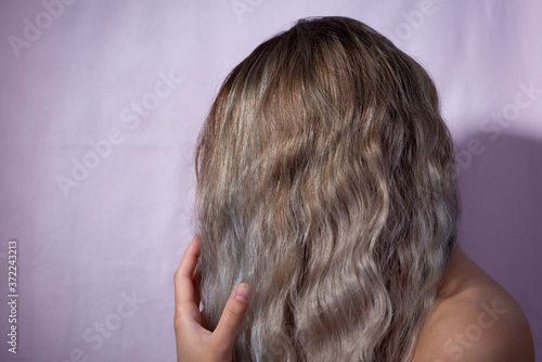 portrait of a girl who covered her face with her hair, lightened after dyeing. On a pink background. cosmetic hair coloring, lightening after colored hair.