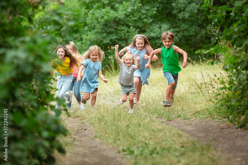 Happiness. Kids, children running on green forest. Cheerful and happy boys and girs playing, laughting, running through green blooming meadow. Childhood and summertime, sincere emotions concept.