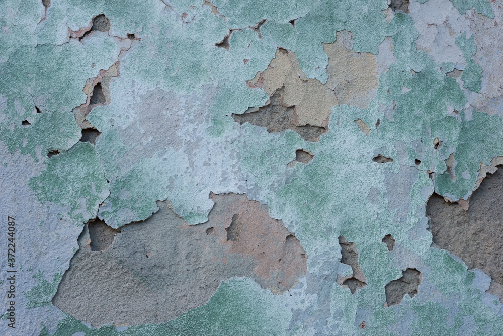 green cracked texture of plaster, with elements of rubbed gray paint. The pastel tone of a textured street wall. Crack in the wall, multiple holes in the old green plaster