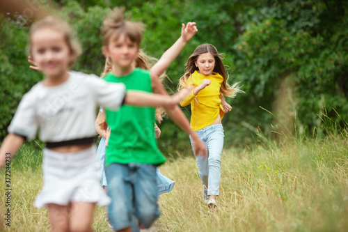 Carefree. Kids  children running on green forest. Cheerful and happy boys and girs playing  laughting  running through green blooming meadow. Childhood and summertime  sincere emotions concept.