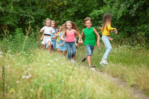 Carefree. Kids, children running on green forest. Cheerful and happy boys and girs playing, laughting, running through green blooming meadow. Childhood and summertime, sincere emotions concept.