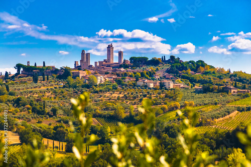Stunning panoramic view of the famous medieval hill town San Gimignano with a close view of the towers piercing the white clouds. It is surrounded by the typical agricultural countryside in Tuscany.