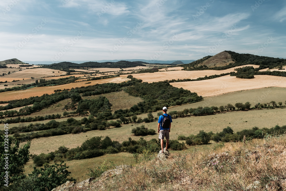 Young man with backpack standing on rock and looking to Czech central mountain valley