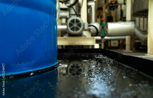 Close up view and low light. Hydraulic oil leak in base tray of blue tank. Inside of the chemical factory.